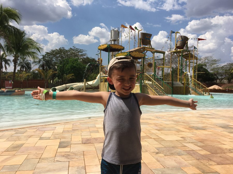 menino de braços abertos em frente a área infantil aquática com escorregadores