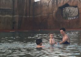 mae e dois filhos pequenos brincando em piscina termal de água escura