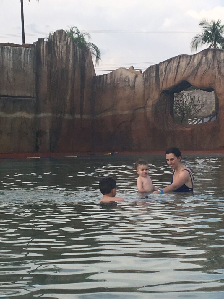 mae e dois filhos pequenos brincando em piscina termal de água escura