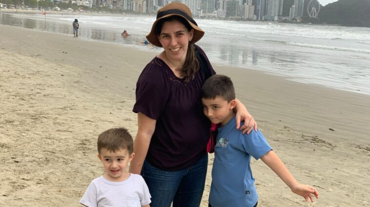 mãe e dois filhos juntos a beira da praia com prédios ao fundo de balneário camboriu
