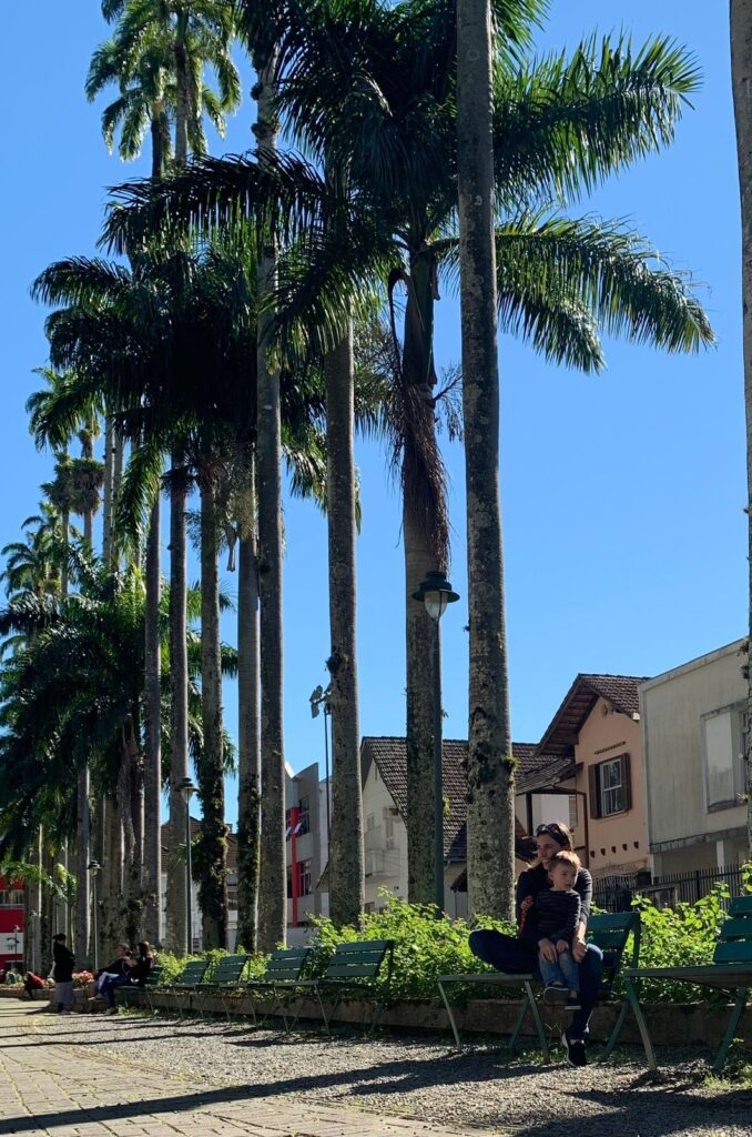 mãe e filho sentados em banco em rua de grandes palmeiras