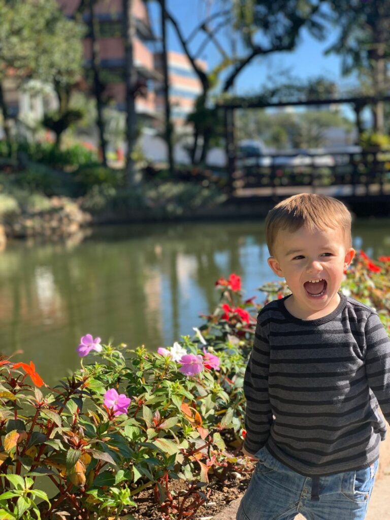 menino rindo em frente a lago e flores