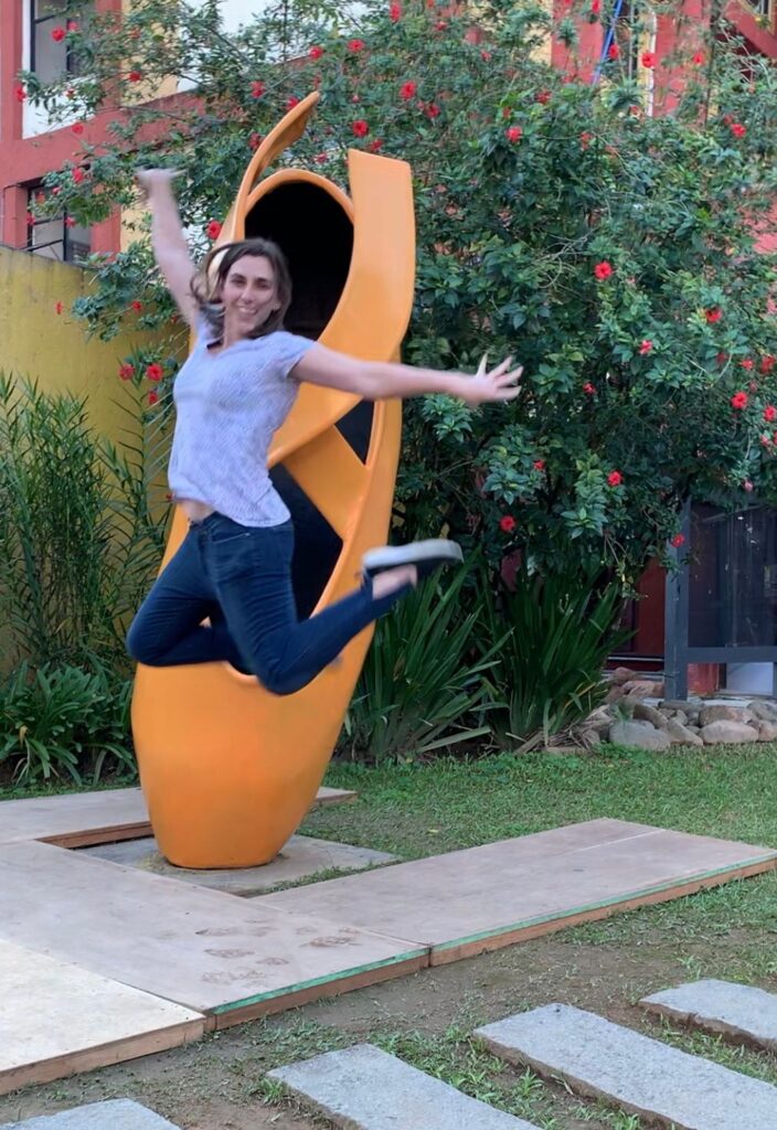 Menina pulando em frente a escultura de sapatilha