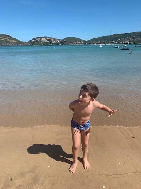 menino mostrando a língua em frente a praia