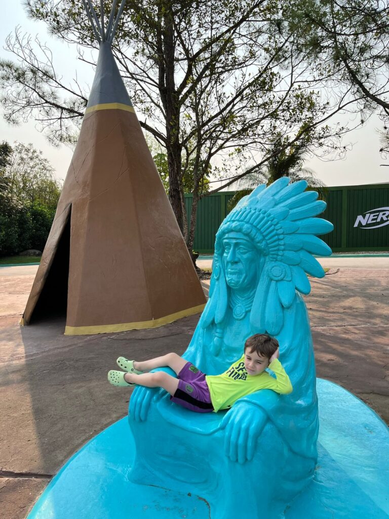 Menino sentado em estátua de índio americano de área temática Beto Carrero