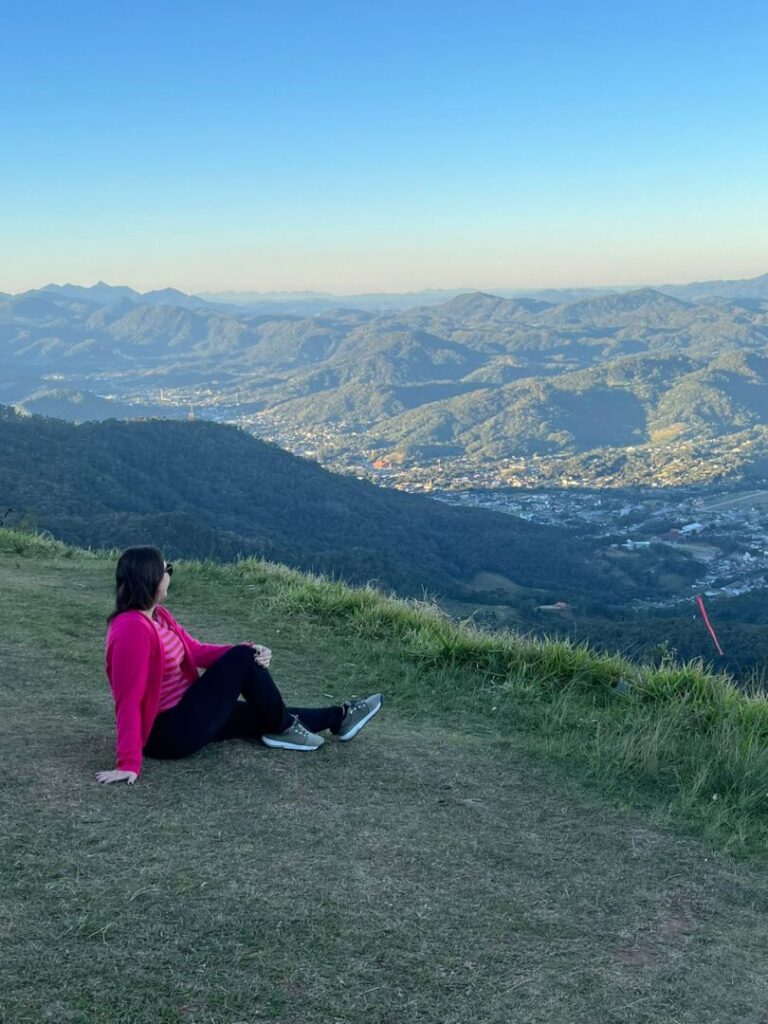 Mulher sentada em alto de morro com serra ao fundo