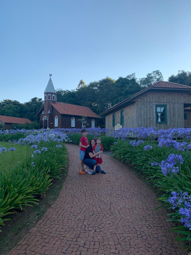 mae e criancas abracados em caminho com flores e igreja e casa de madeira ao fundo