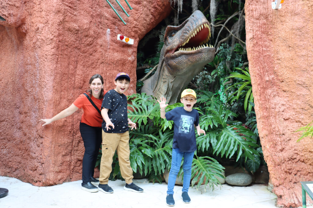 mulher e dois meninos em cenário com t-rex