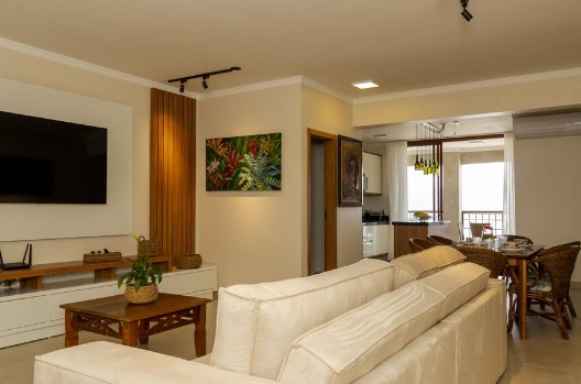 sofá de costas em sala com TV, decoração mesa e cozinha ao fundo