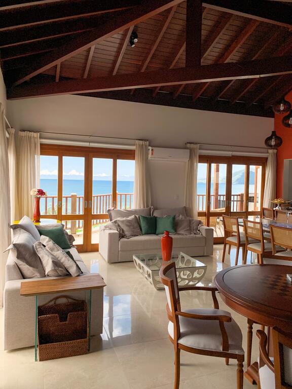 Sala ampla com dois sofás e mesa pequena para xadrez fundo da foto com janelas grandes com vista para o mar