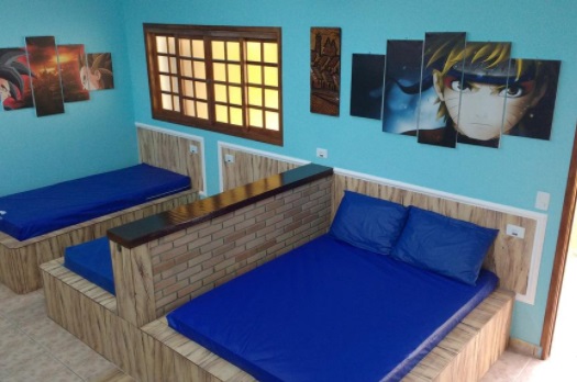 quarto de parede azul com quadros de personagens de desenhos japoneses e 1 cama de casal e duas de solteiro