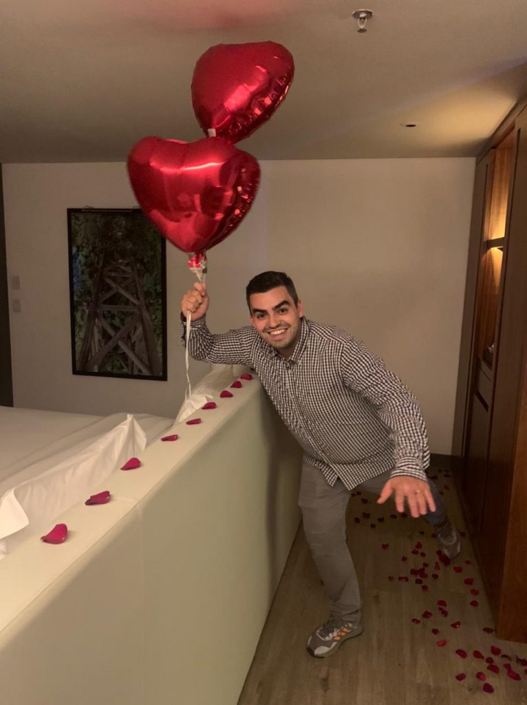 homem pulando em quarto decorado com balões de coração e pétalas de rosas