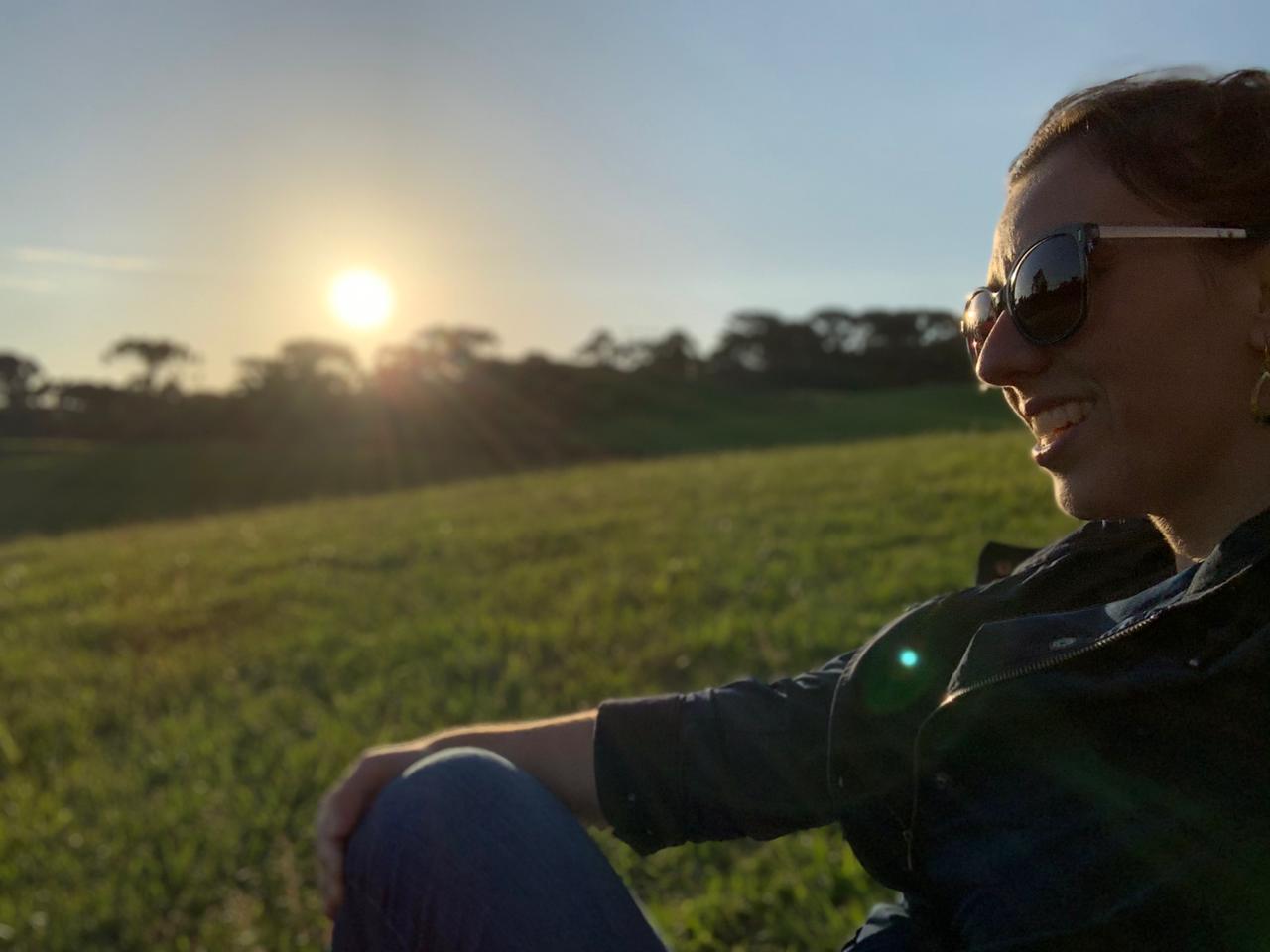mulher sentada na grama de lado com pôr do sol
