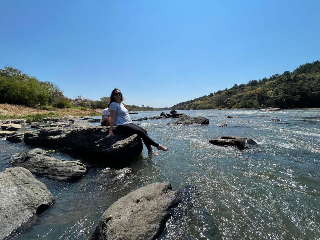 mulher sentada em ponta de uma pedra e visão ampla do rio