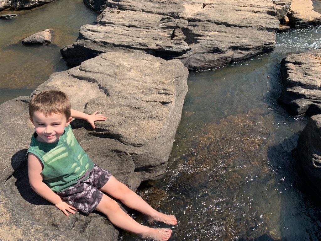 criança com pés no rio sentada em uma pedra