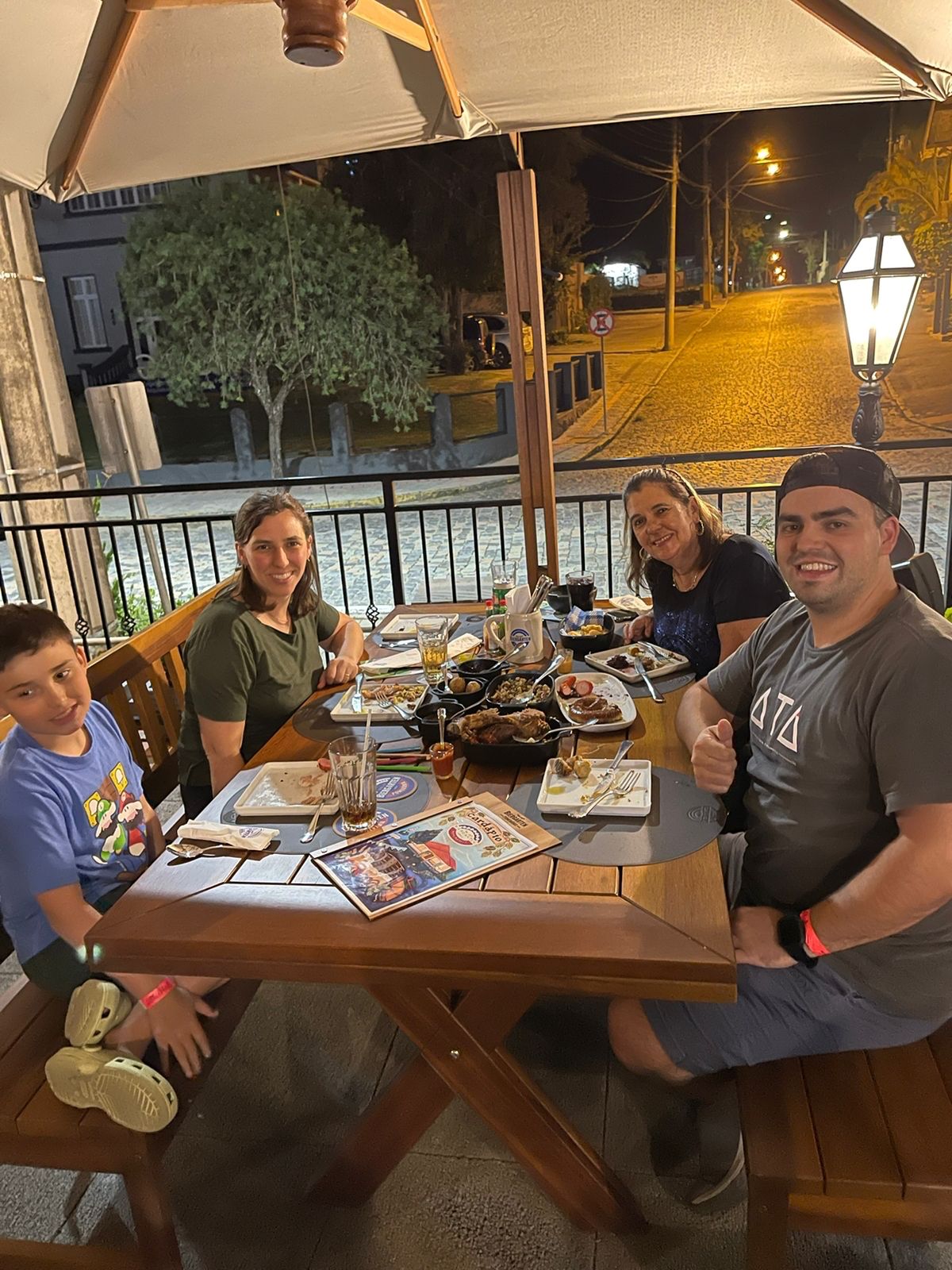 Família com 4 pessoas sentada em mesa ao ar livre a noite