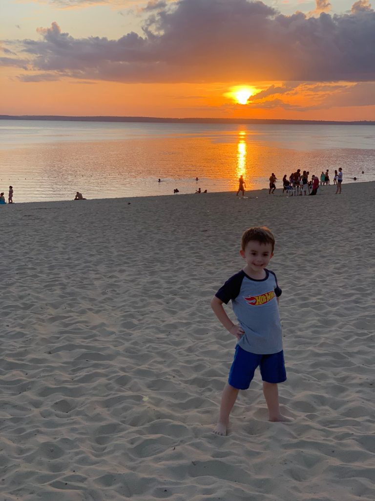 menino em frente a areia e praia no rio com pôr do sol no fundo