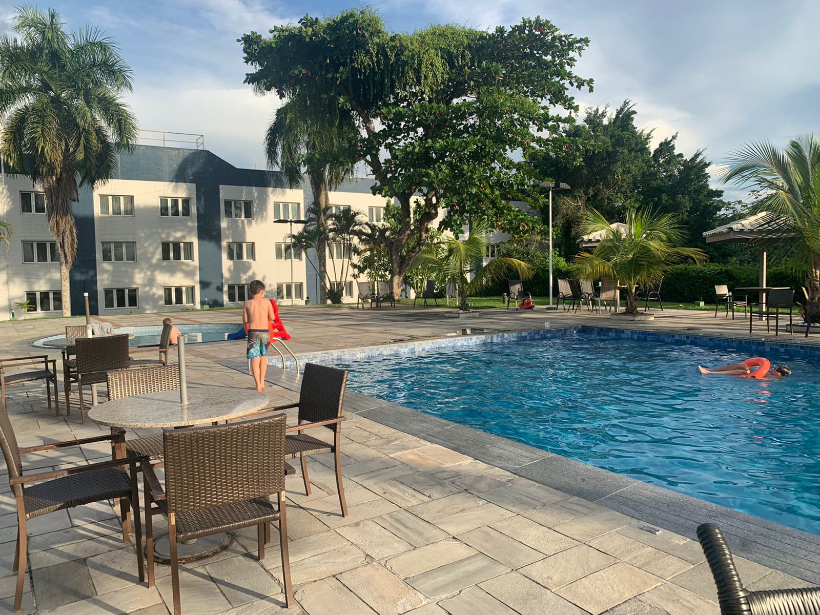 piscina retangular com palmeiras e prédio de hotel ao fundo