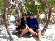 casal sentado dentro de arco em formato de coração na praia