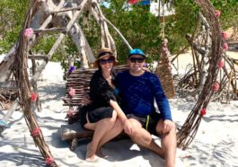 casal sentado dentro de arco em formato de coração na praia