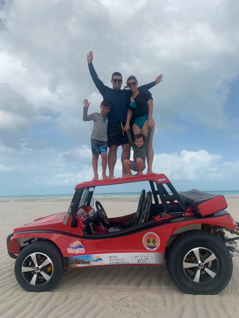 Família em pé em cima de um buggy com praia no fundo