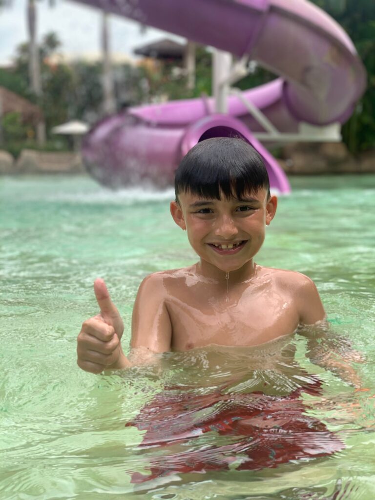 menino dentro de piscina fazendo sinal de positivo