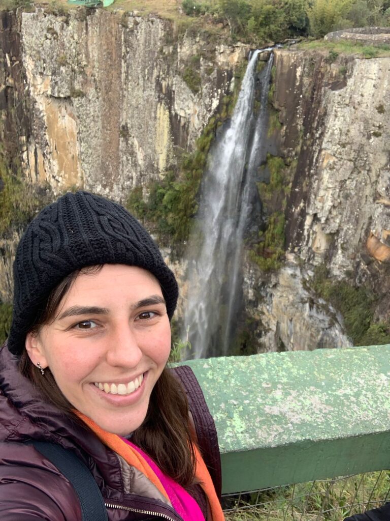 Selfie de mulher com cachoeira entre grande paredão ao fundo