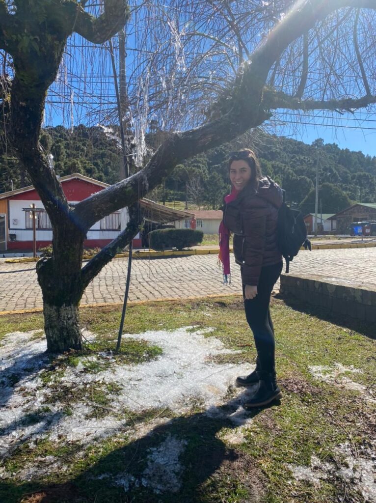 mulher em pé sorrindo ao lado de árvore com com cristais de gelo