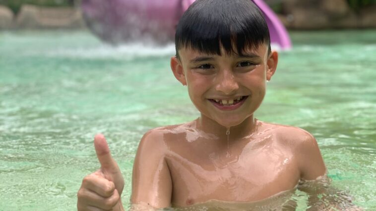 menino dentro da água fazendo sinal de positivo com a mão