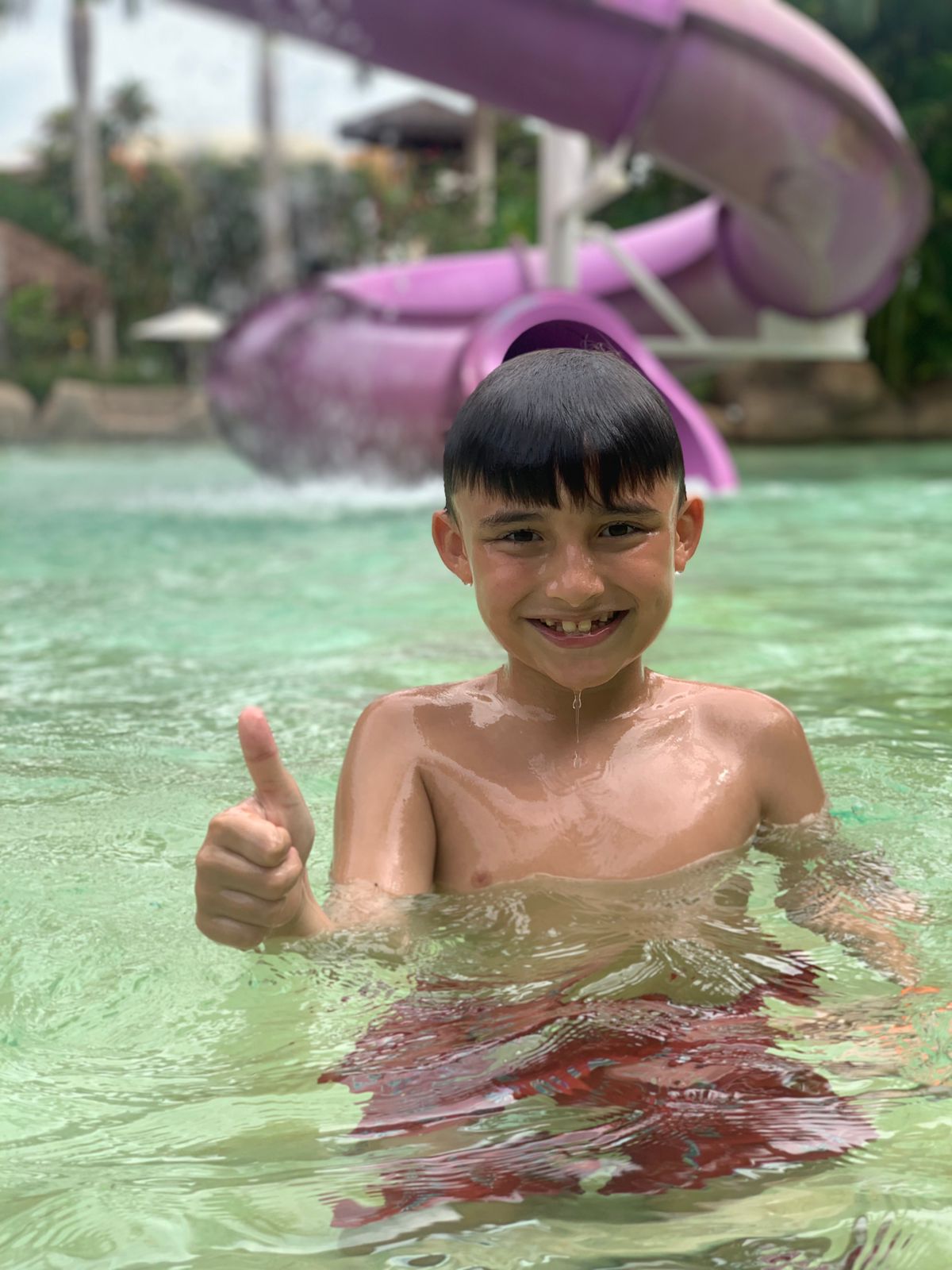 menino dentro da água fazendo sinal de positivo com a mão