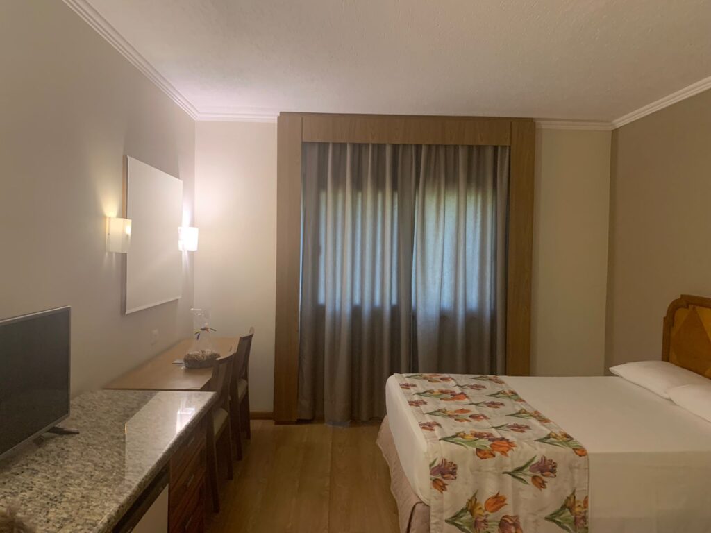 quarto de hotel mostrando cama, tv no balcão e janela ao fundo