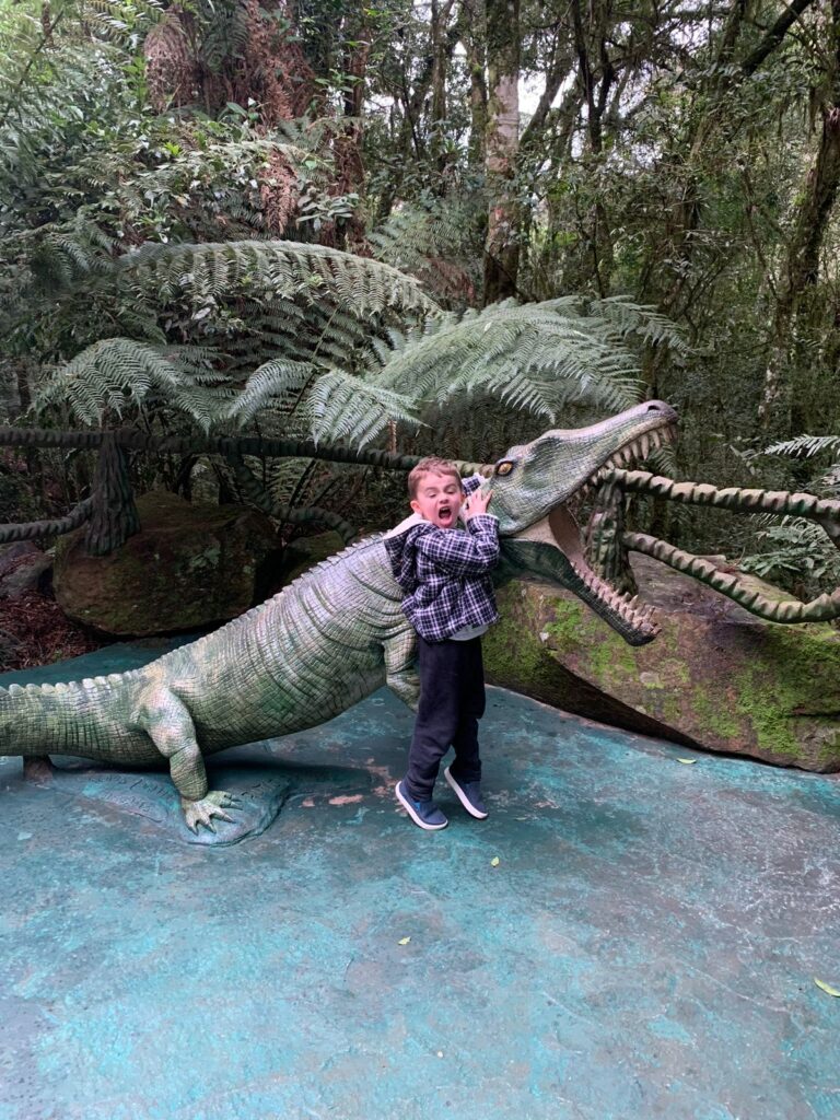 menino junto com estátua de dinossauro