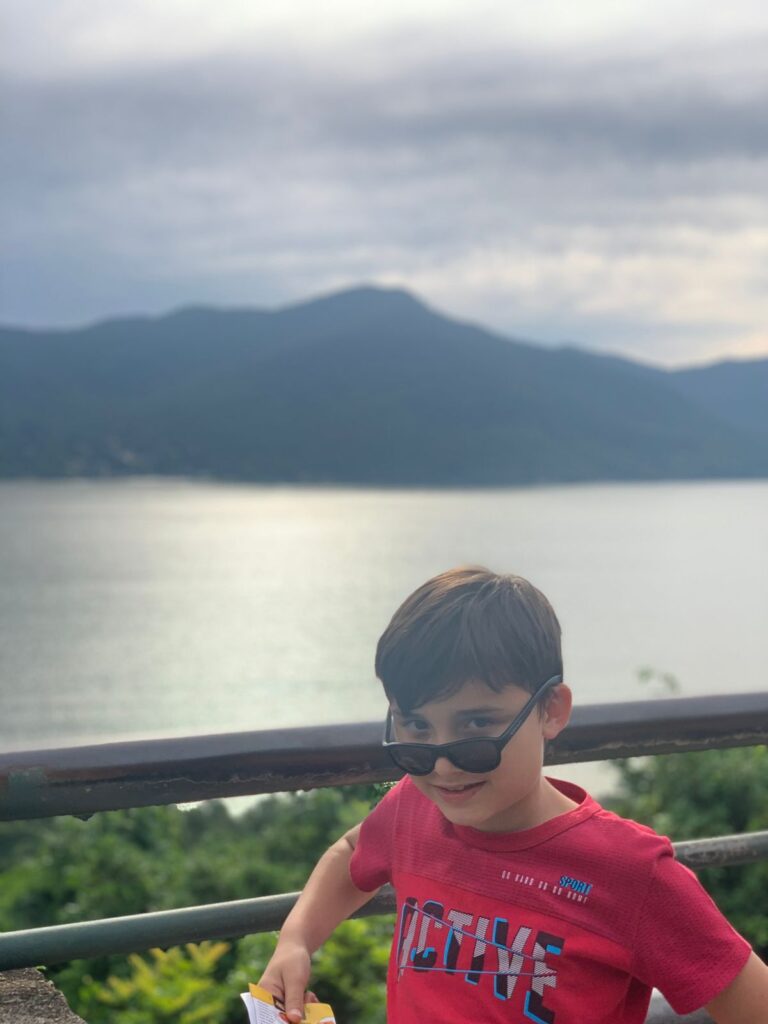menino de óculos fazendo pose com vista ao fundo de lagoa e montanha