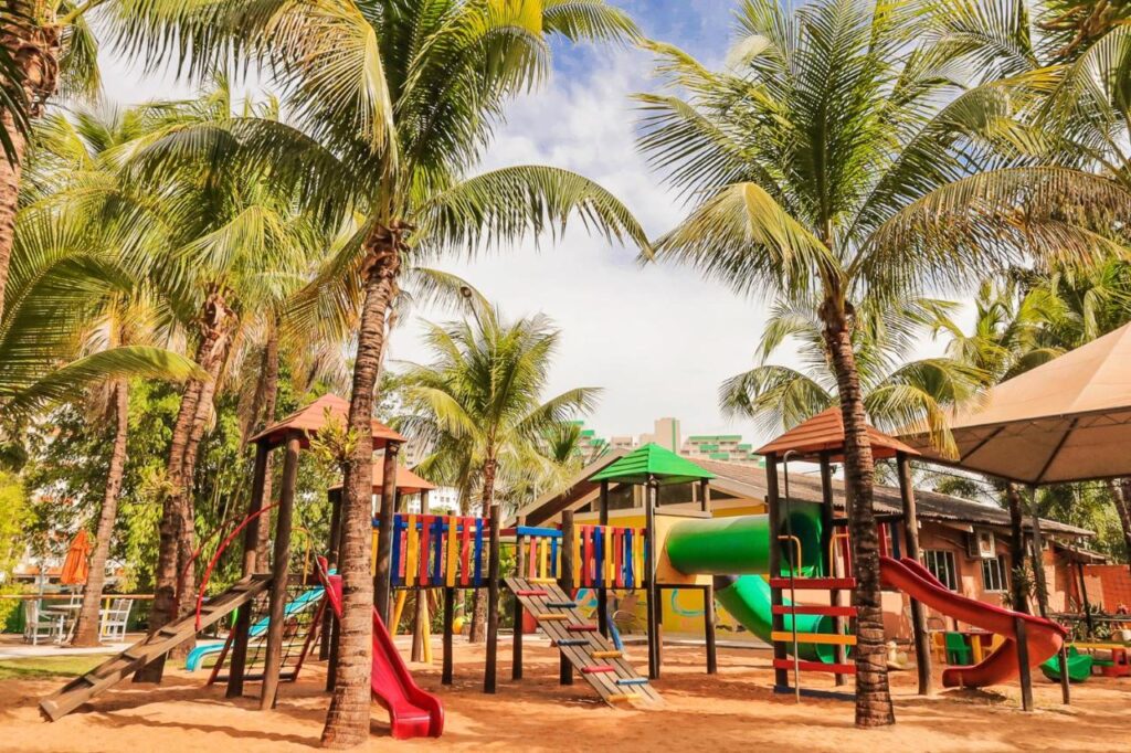 Parque infantil em cima de areia e coqueiros ao redor