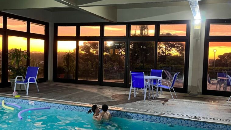 piscina coberta com janelas mostrando pôr do sol ao fundo