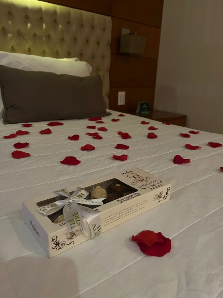 cama com caixa de chocolate e pétalas