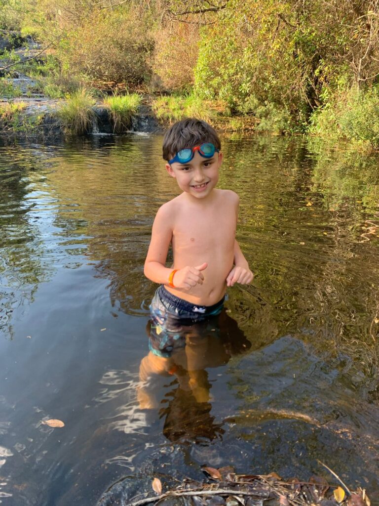 menino dentro de rio e natureza ao redor