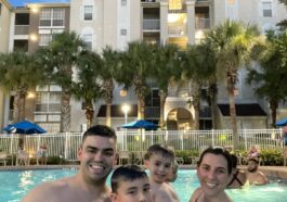 mãe, pai e dois meninos dentro de piscina com prédio de hotel no fundo