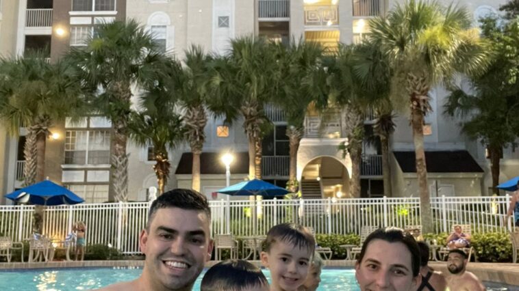 mãe, pai e dois meninos dentro de piscina com prédio de hotel no fundo