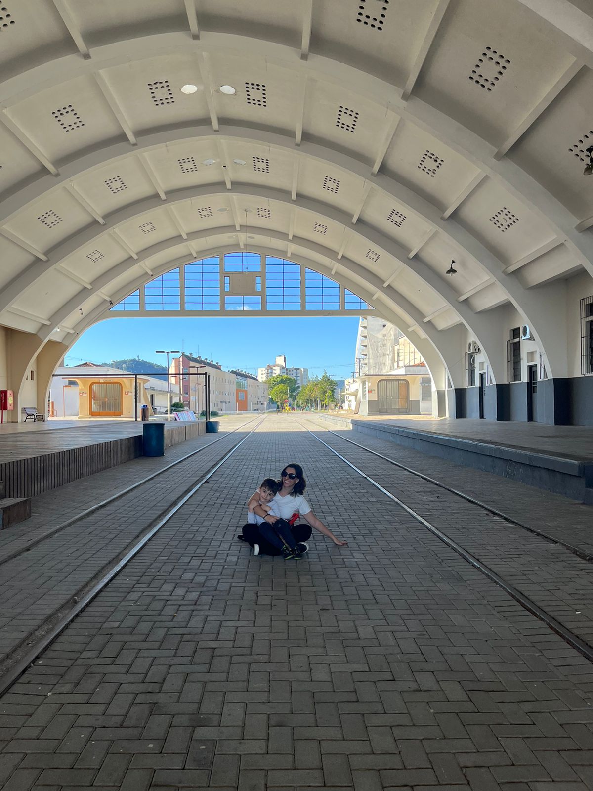 mãe e menino sentados em estação de trem inativa junto aos trilhos