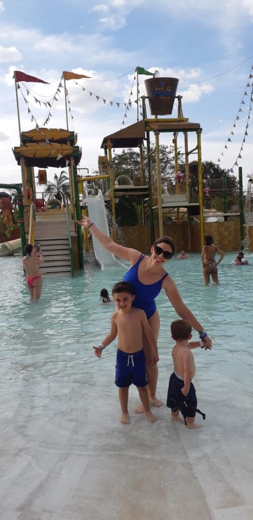 mãe e dois meninos em frente a brinquedo aquático em piscina rasa