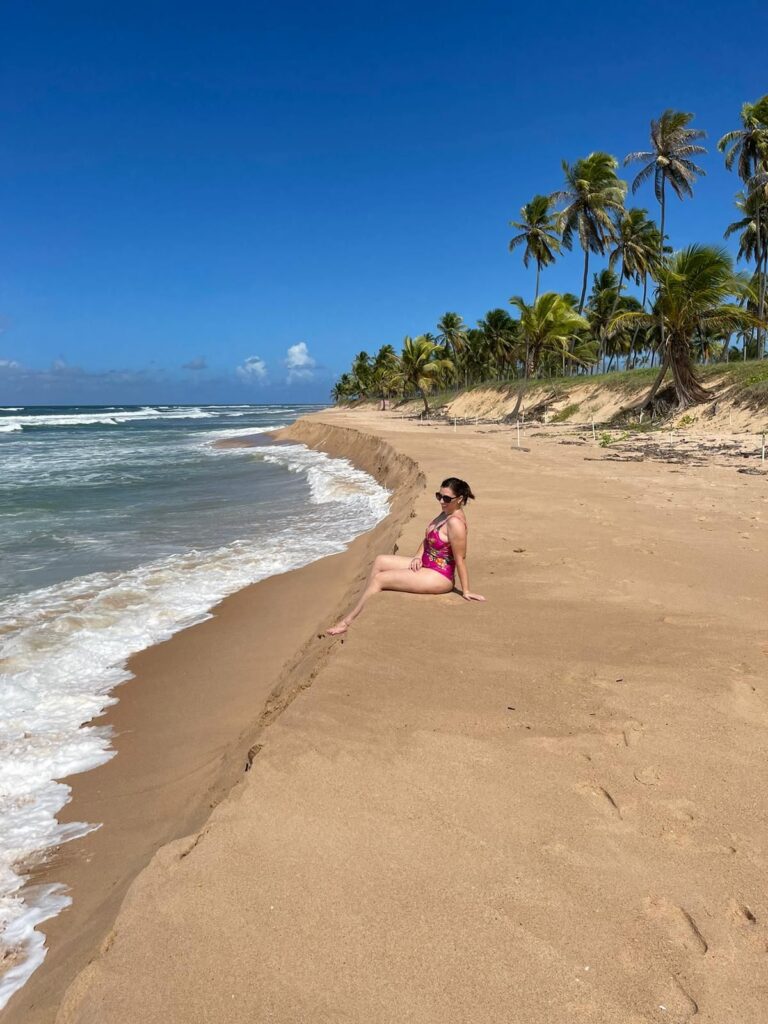 mulher em praia com coqueiros sentada em morro de areia