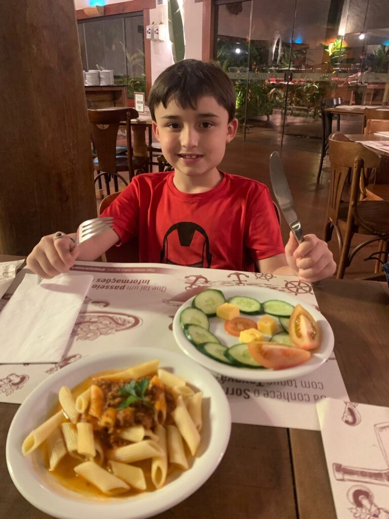 menino sentado em mesa para jantar salada e macarrão
