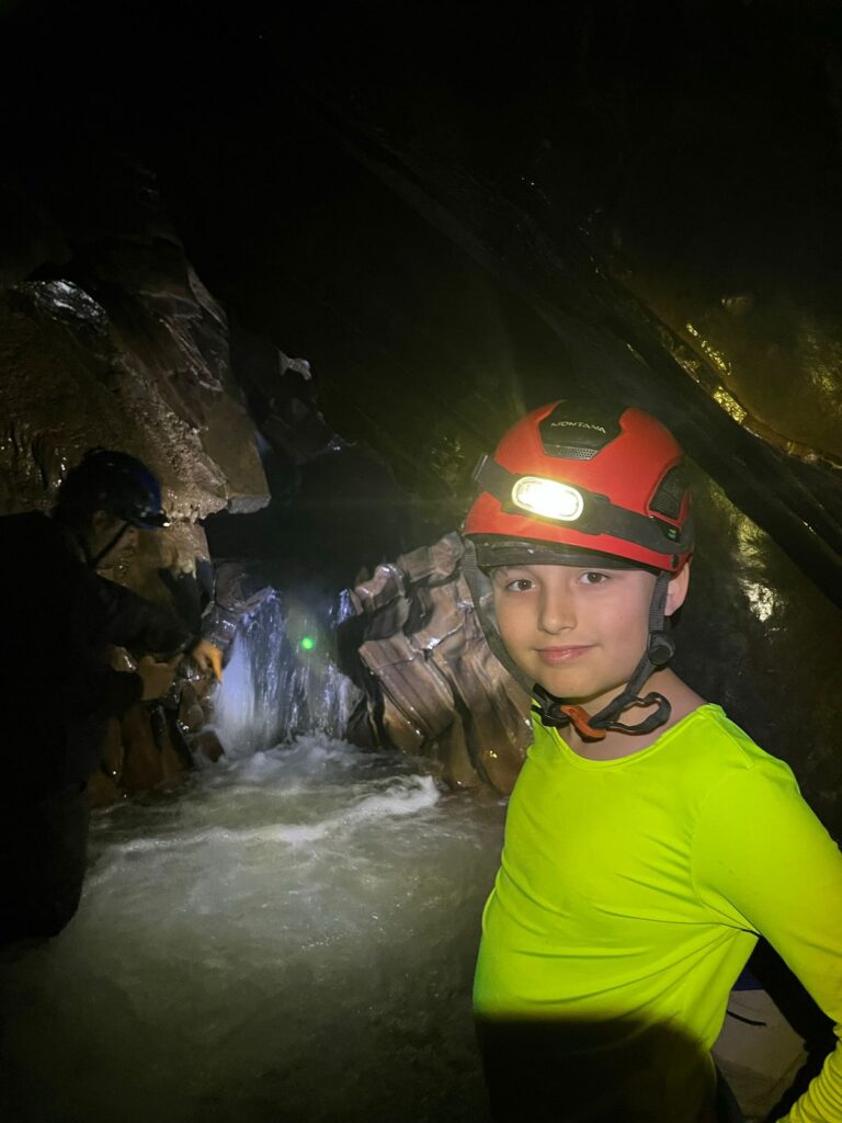 menino usando capacete dentro de caverna com pequena cachoeira dentro