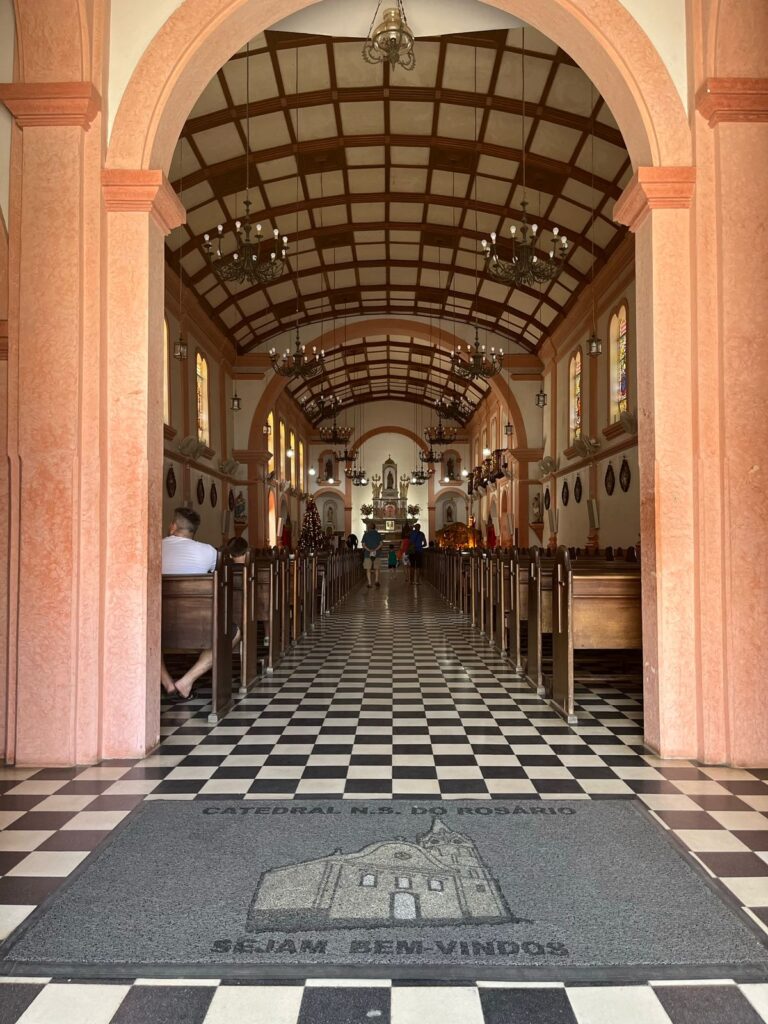 entrada de igreja católica grande com colunas rosadas e piso quadriculado em preto e branco