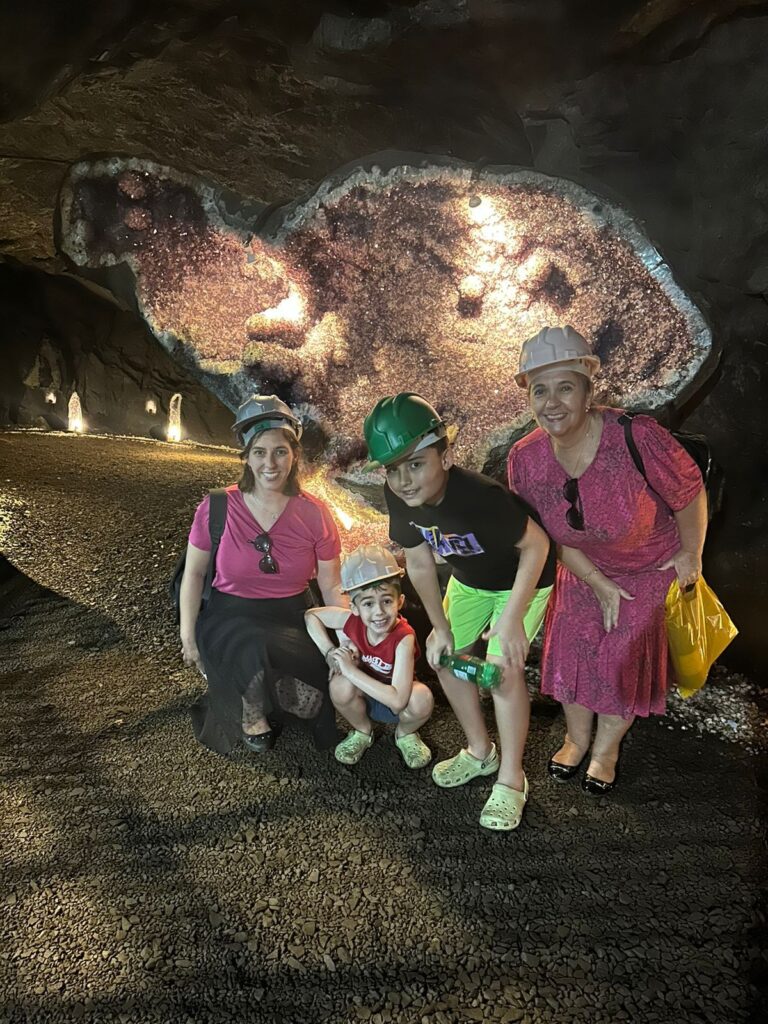 duas mulheres e dois meninos abaixados dentro de mina com pedra grande ametista no fundo