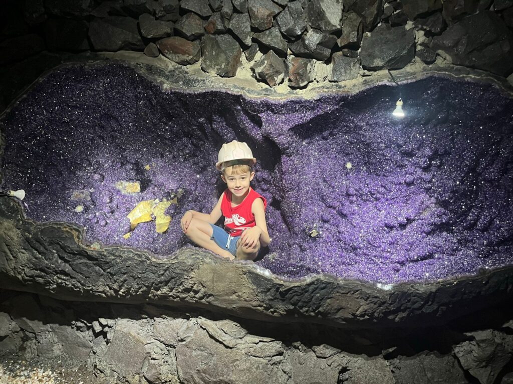 menino sentado dentro de grande pedra ametista em uma mina