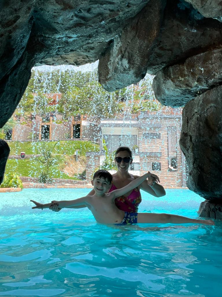 mãe e filho dentro de piscina com cascata ao fundo