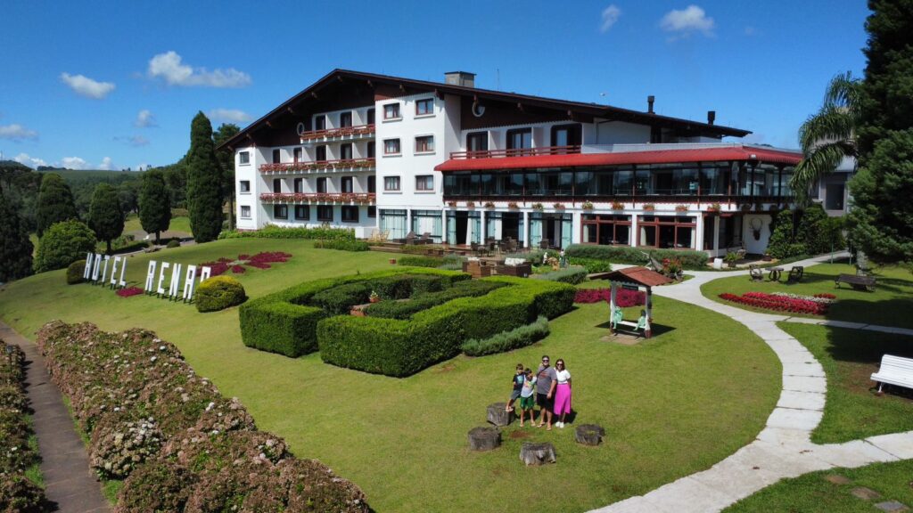 Imagem aérea de família em grande gramado e fachada em estilo alemão de hotel