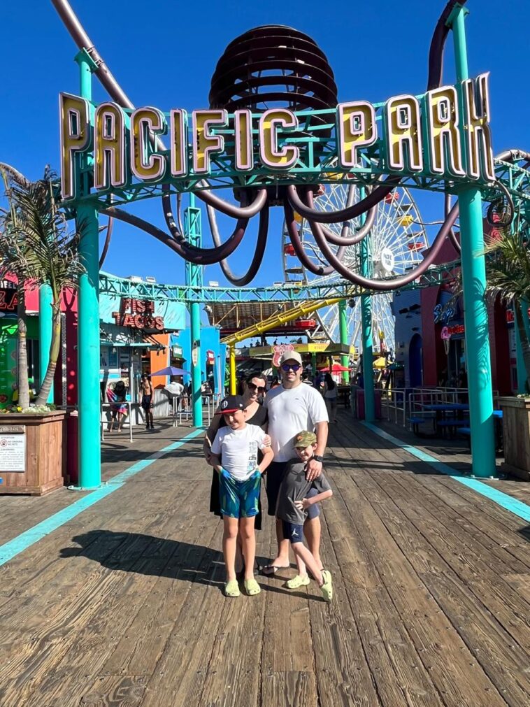 Pai, mãe e dois meninos em frente a entrada de parque de diversões